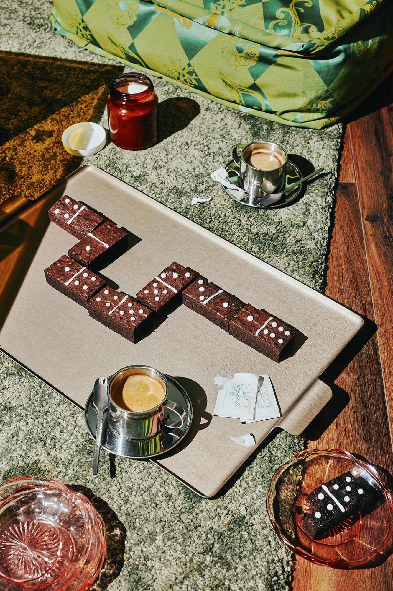 Brownie pieces decorated with white dots like dominoes, arranged on a tray next to espresso cups and a candle