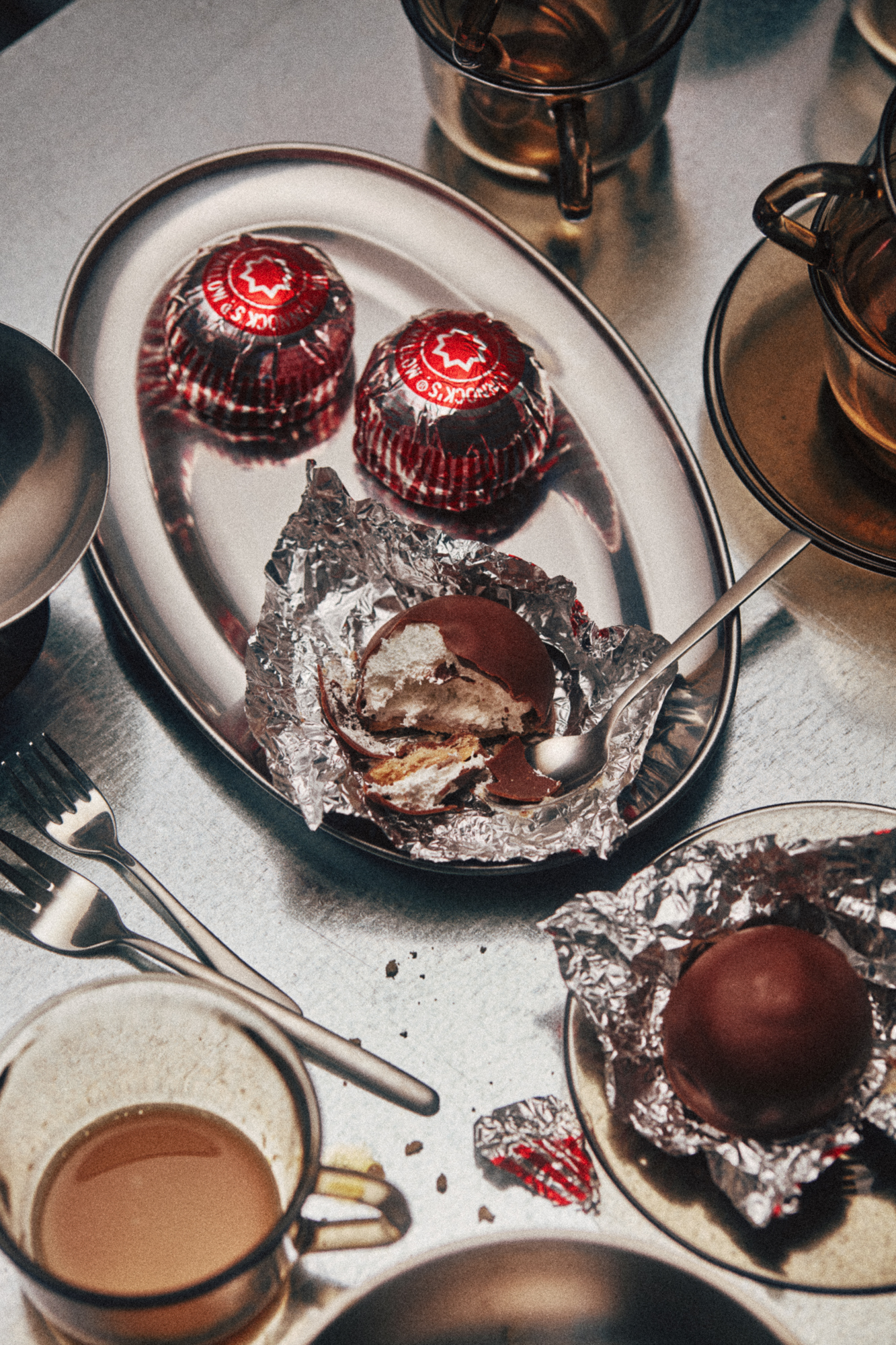 Overhead view of a plate with two chocolate truffles and a half-eaten praline in foil, coffee cups in the background