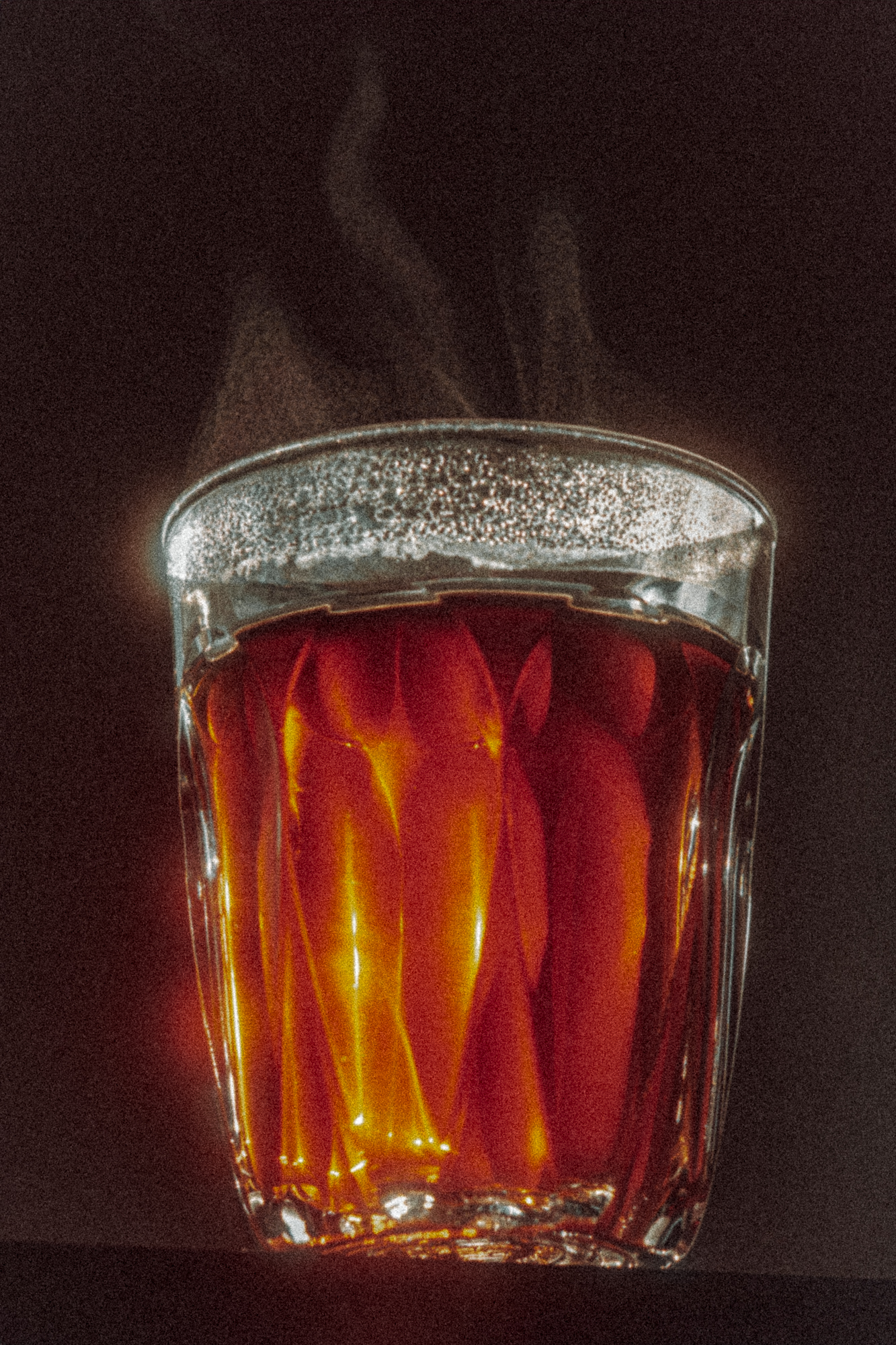 Close-up of a steaming glass of tea backlit and glowing orange-red