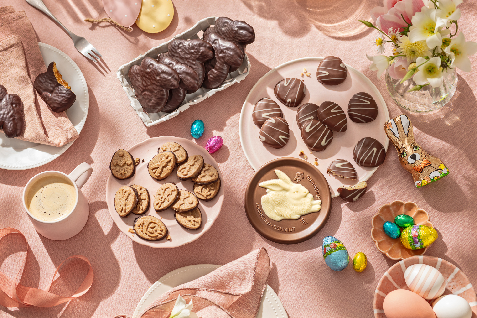 Overhead view of an Easter table with chocolate bunnies, decorated eggs, gingerbread, foil-wrapped eggs and a bouquet of flowers