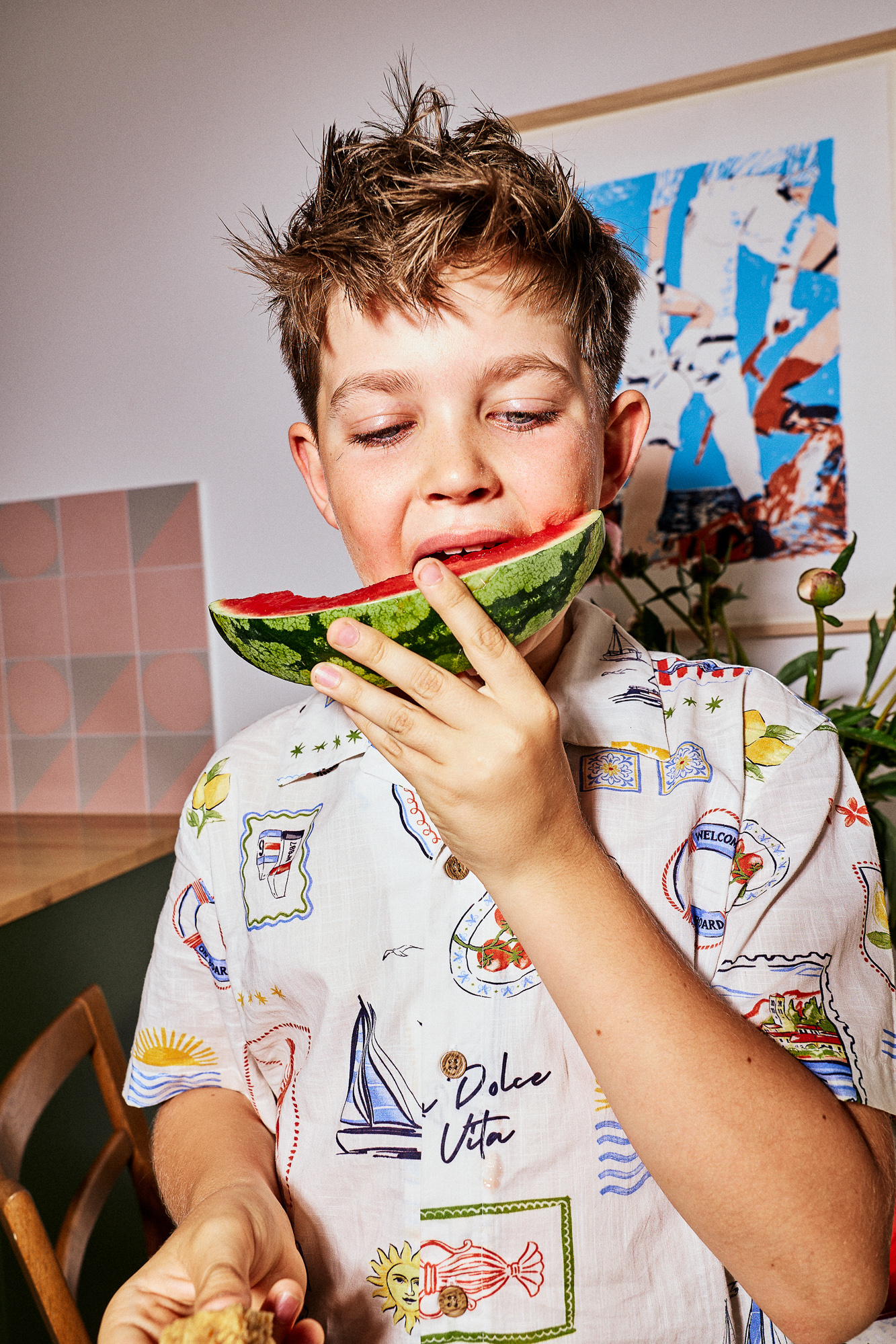 Boy in a patterned shirt biting into a slice of watermelon