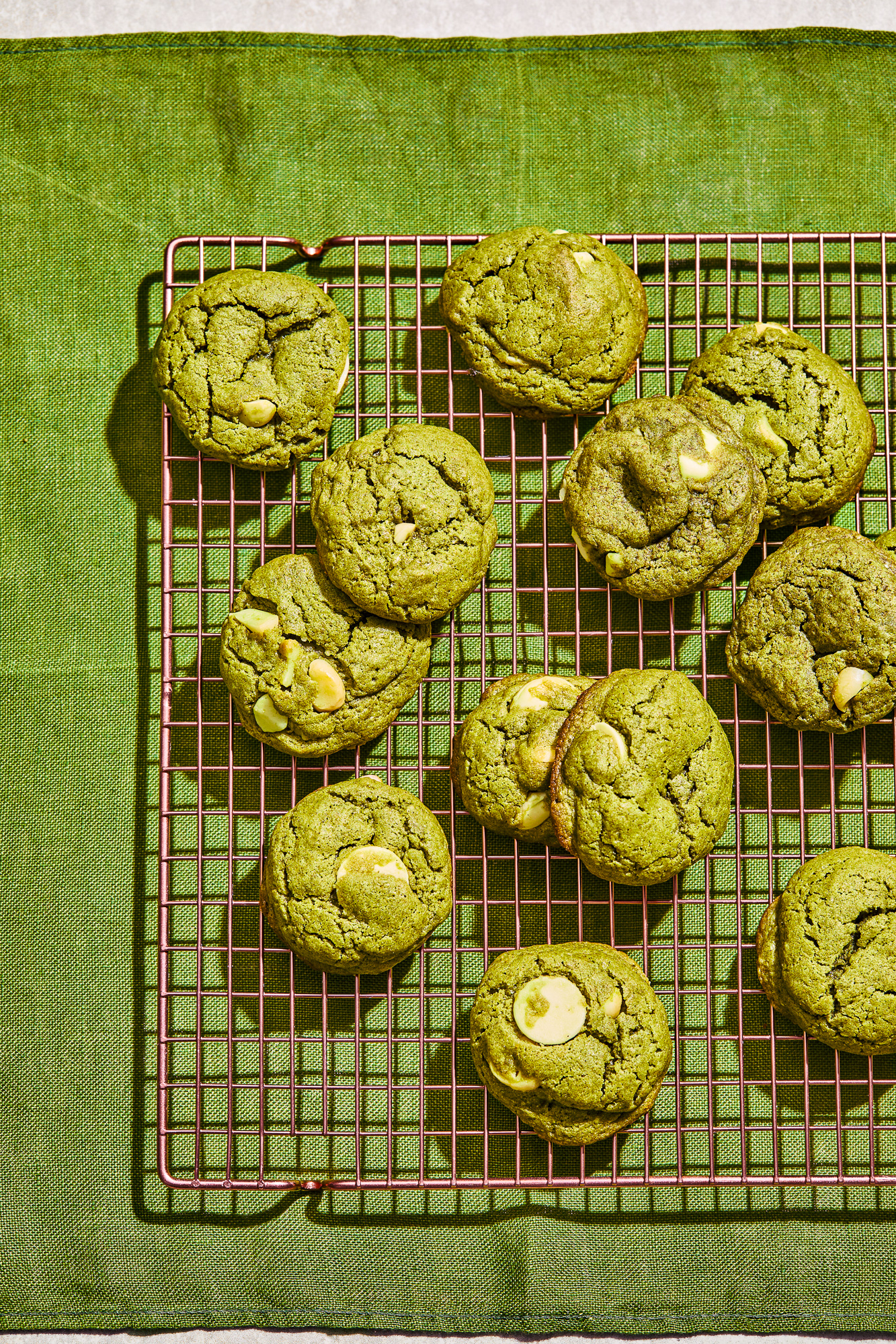 Overhead view of freshly baked green matcha cookies with white chocolate on a cooling rack