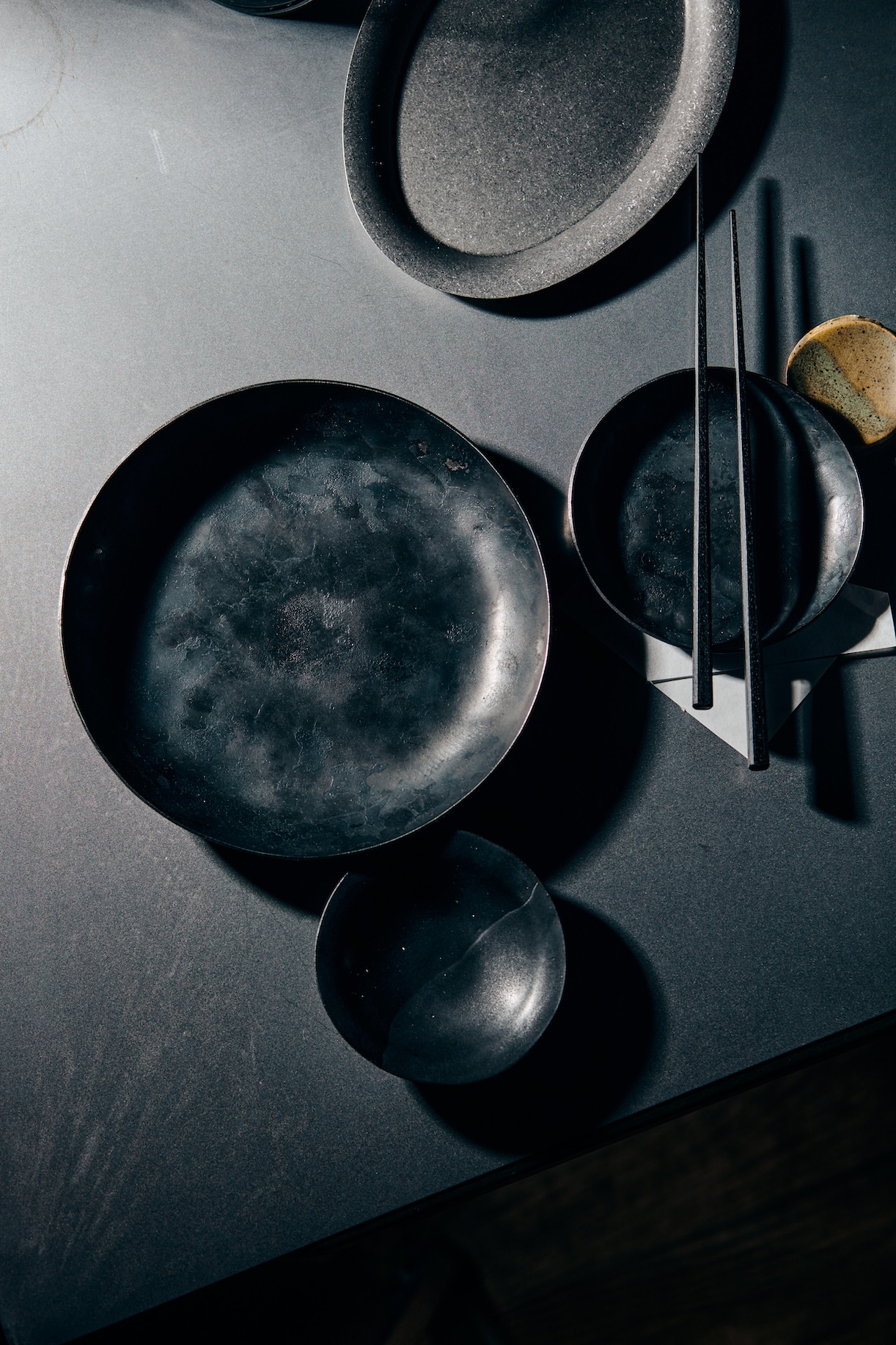 Still life of dark, irregularly shaped ceramic plates and chopsticks on a black surface