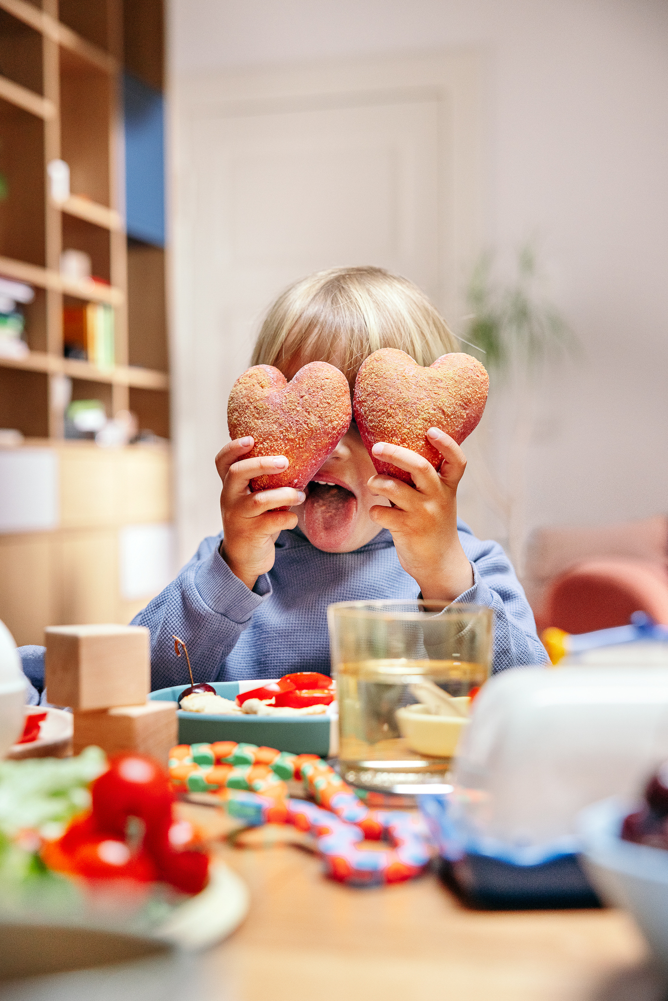 Child holding two heart-shaped red rolls over their eyes like glasses and sticking out their tongue