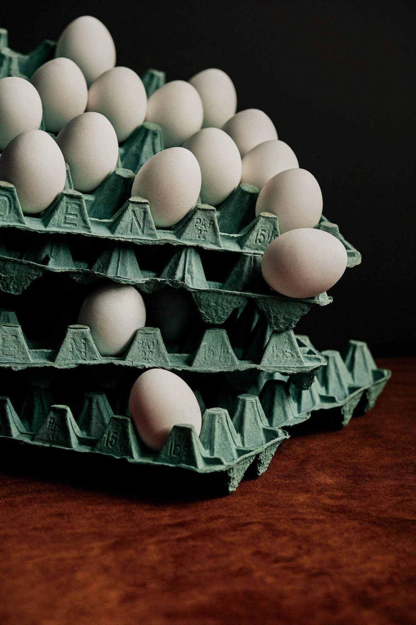 Stacked egg cartons with white eggs, some loose on a dark wooden table