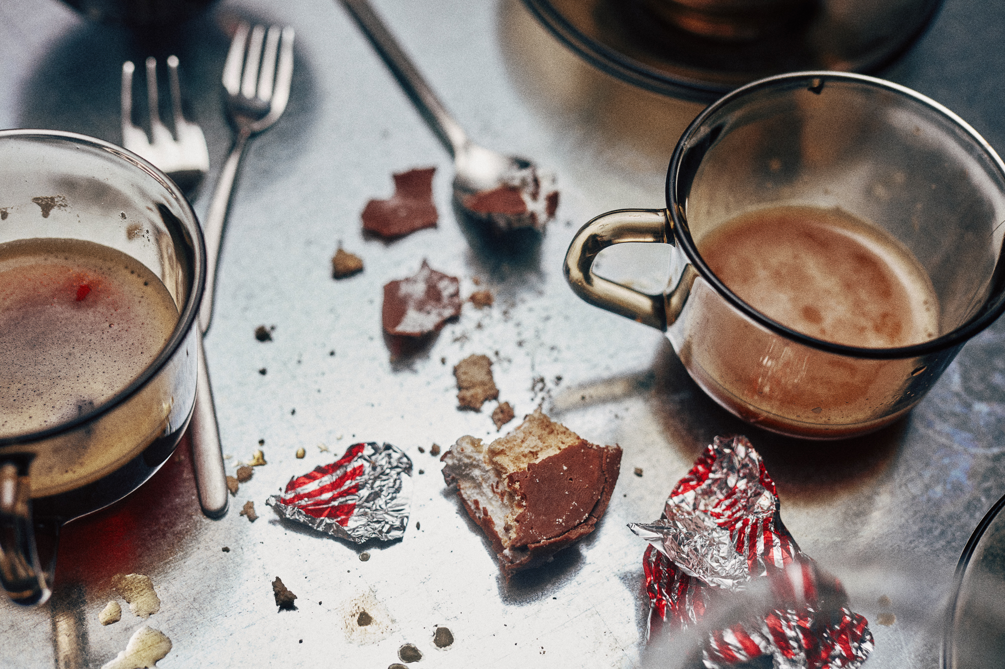 Close-up of empty coffee cups and chocolate wrappers with red foil on a tabletop