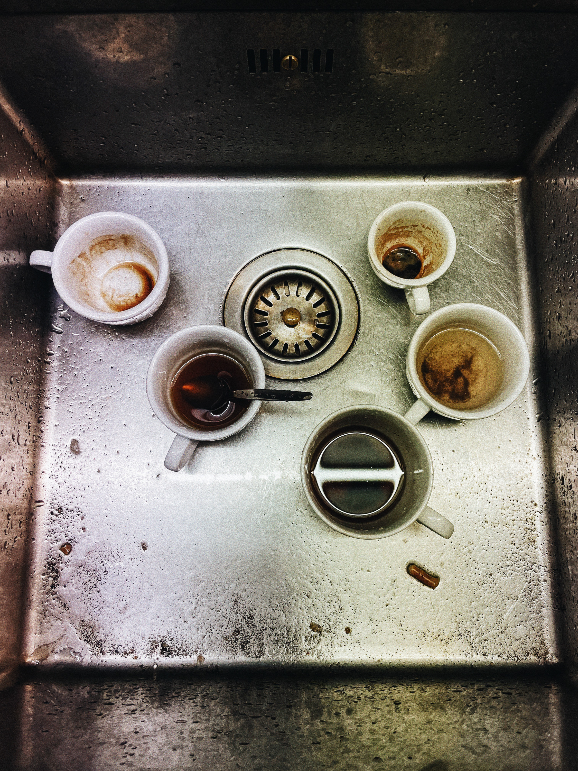 Overhead view into a sink filled with used coffee and tea cups