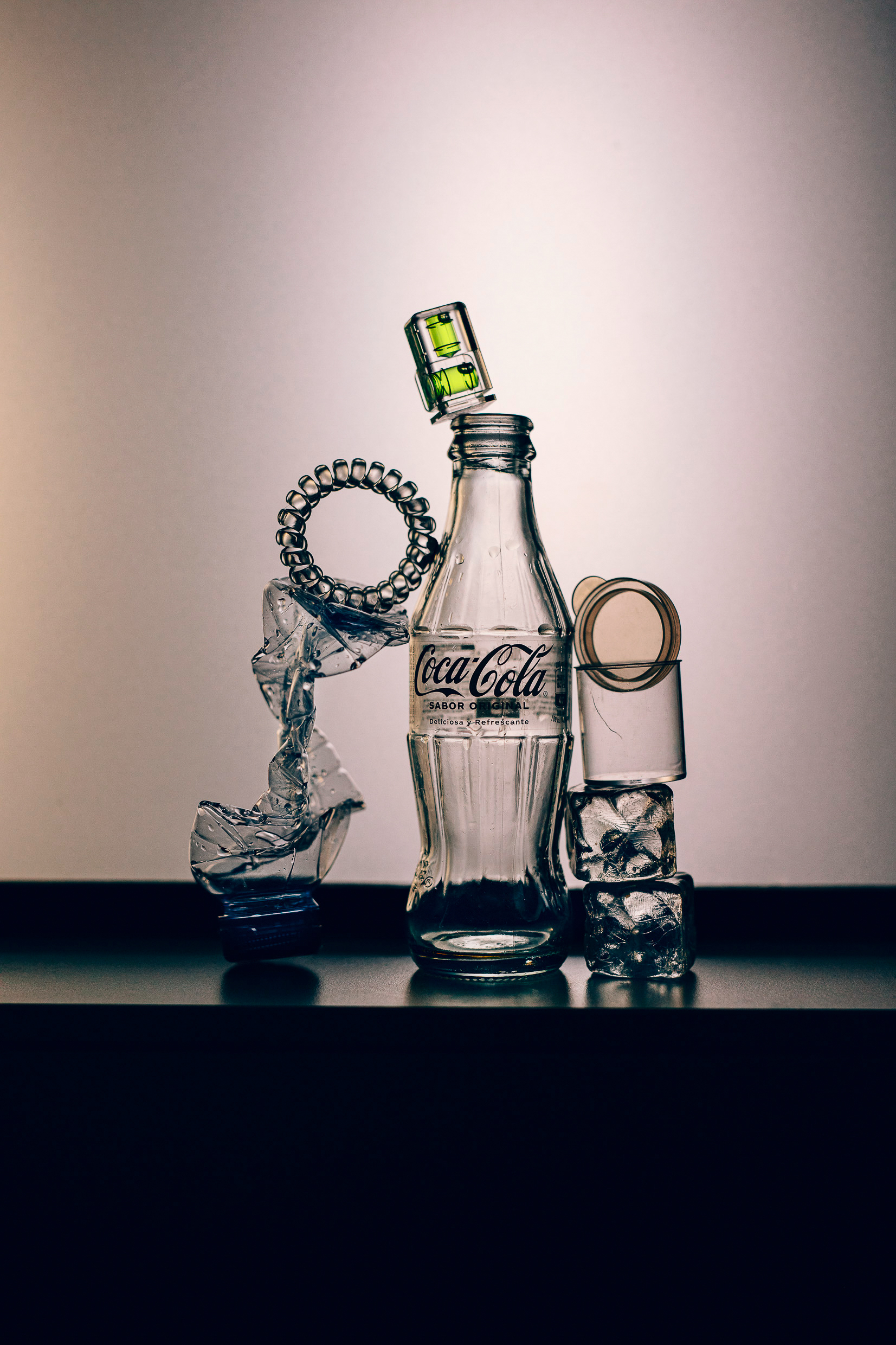 Still life with an empty Coca-Cola glass bottle, ice cubes, a spirit level and crumpled plastic against a bright background