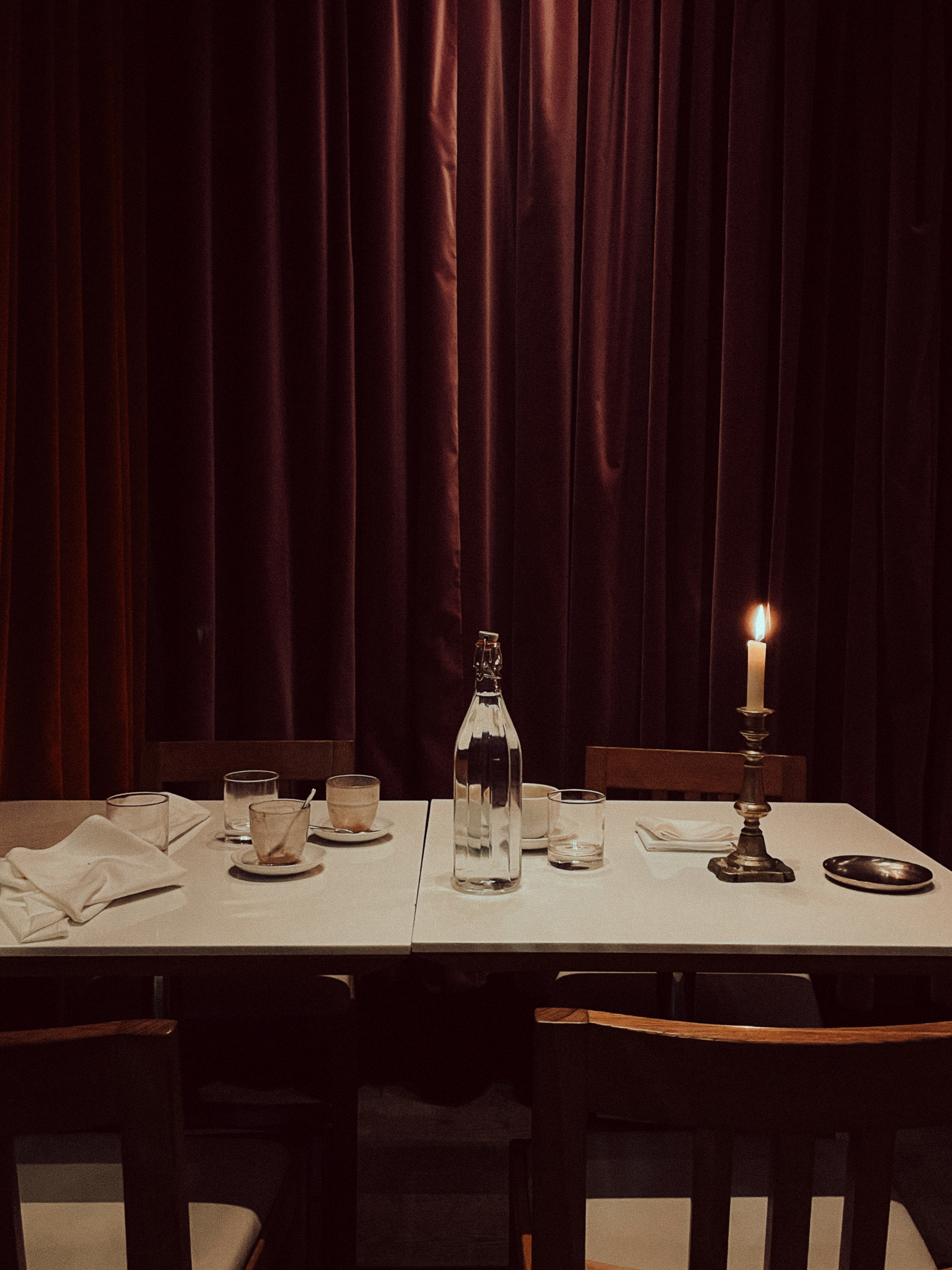 Table set with a water bottle, glasses and a lit candle against a burgundy curtain